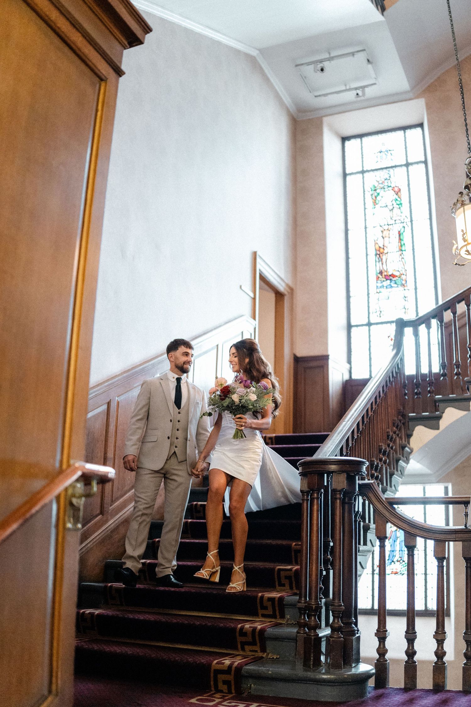 A couple poses for romantic photos on a wooden staircase with stained glass windows in the background.