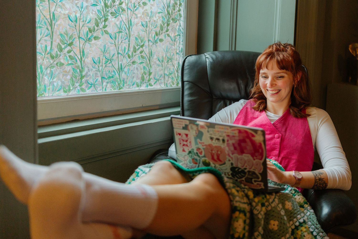 Person relaxing on couch near window with floral wallpaper.