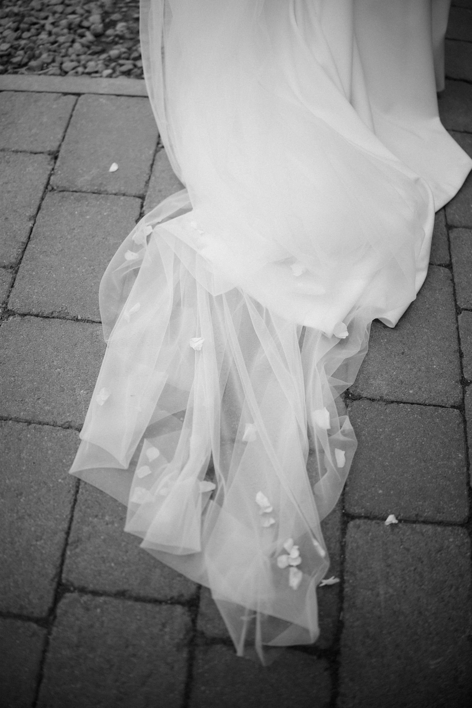 Close-up black and white photo of flowing wedding dress train on stone pavement.