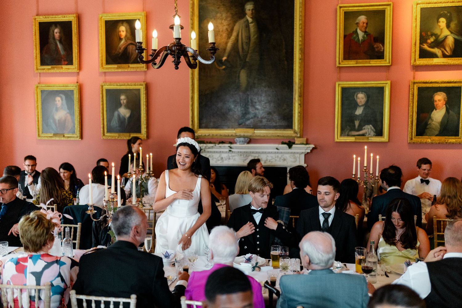Formal dining room with pink walls adorned with historic portraits and elegant chandeliers.