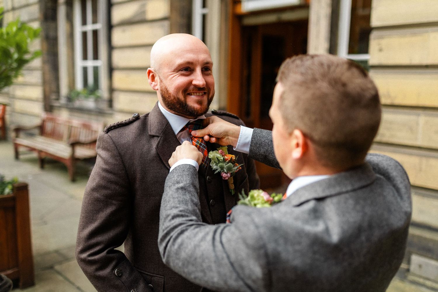 Wedding party members share joyful moments outside a historic stone building.