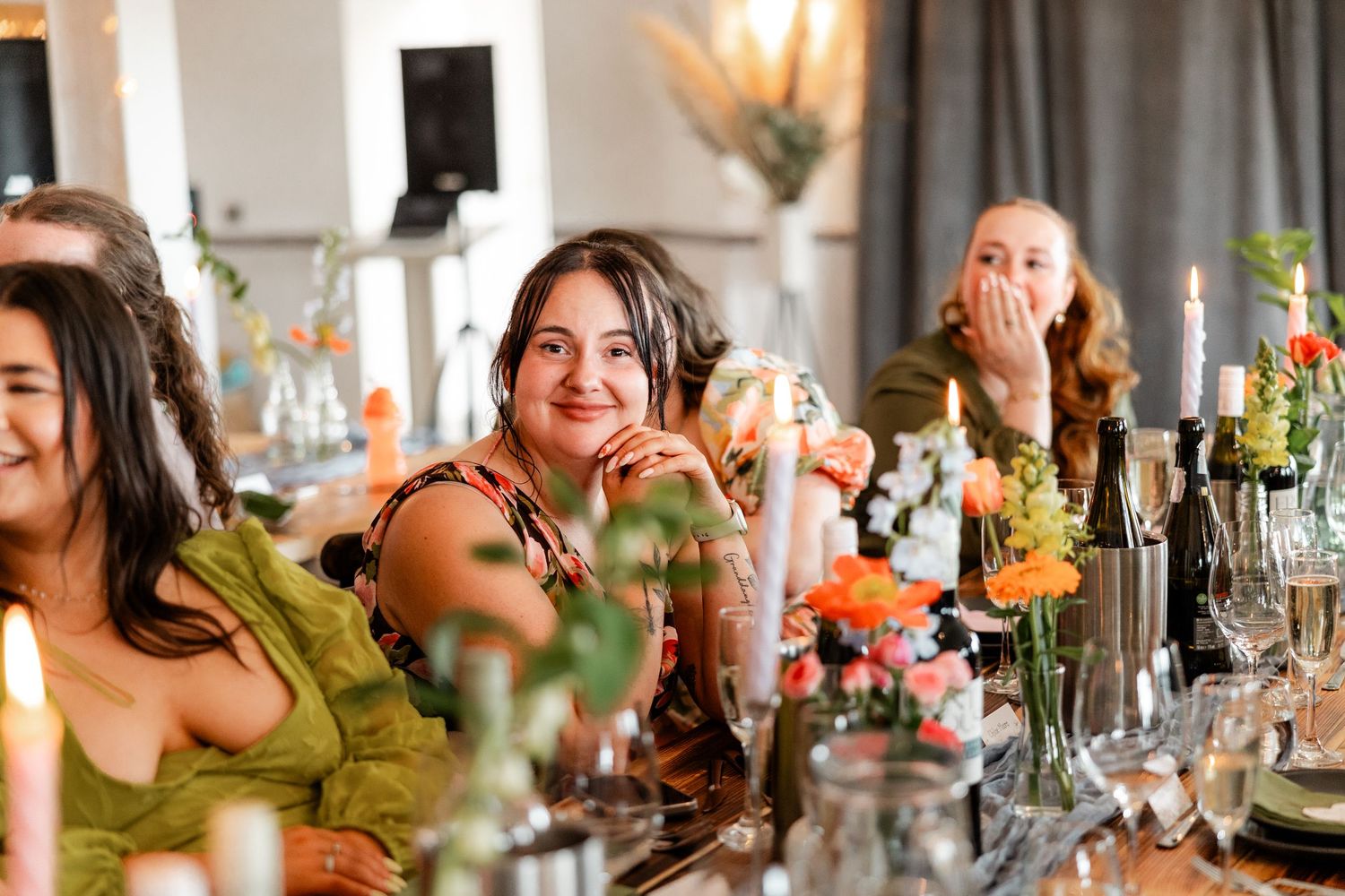 Long dining table decorated with colorful floral centerpieces and candles at wedding reception.