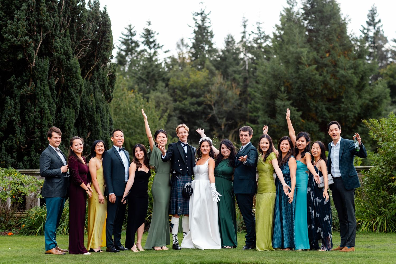 Wedding party members in vibrant attire pose together in outdoor garden.