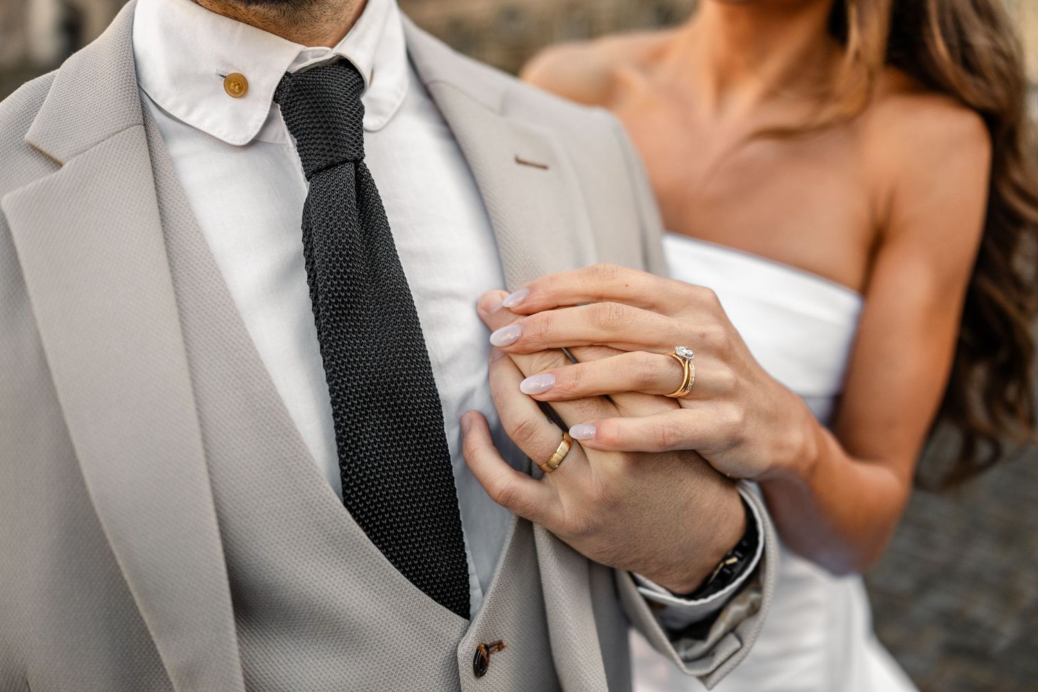 Close-up of wedding ring and light grey suit with black tie detail.