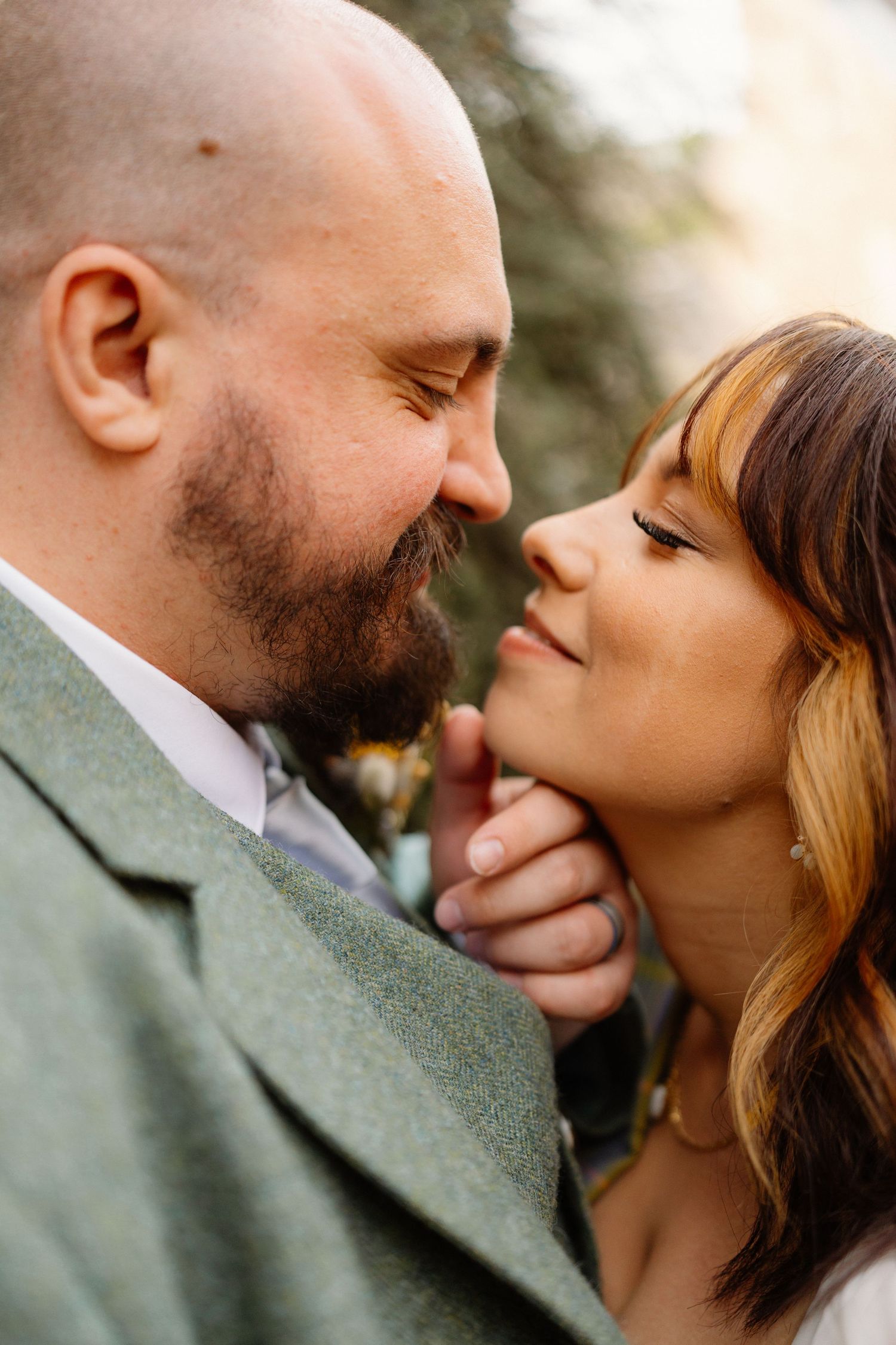 Close-up of a couple sharing a tender moment, groom in green suit leaning toward smiling bride.