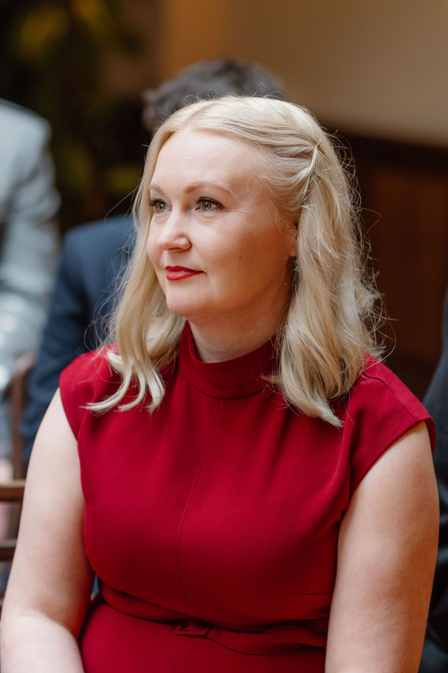 Elegant blonde woman in red sleeveless dress with red lips at formal event.