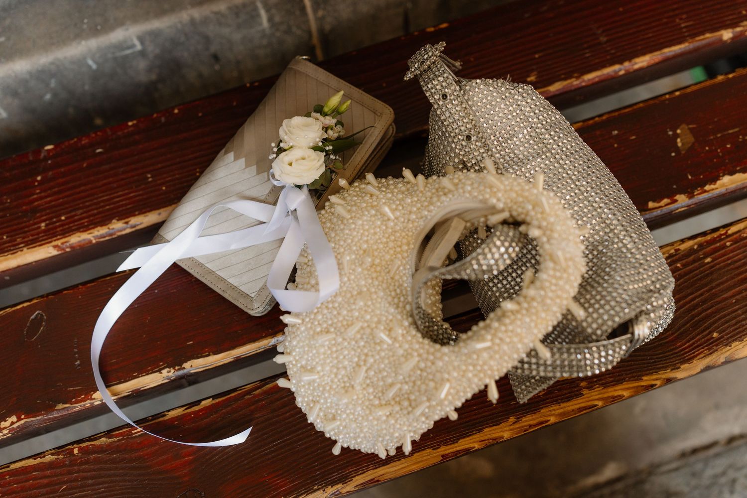 Wedding accessories on wooden bench featuring pearl heart, bouquet, rings, and burlap bag.
