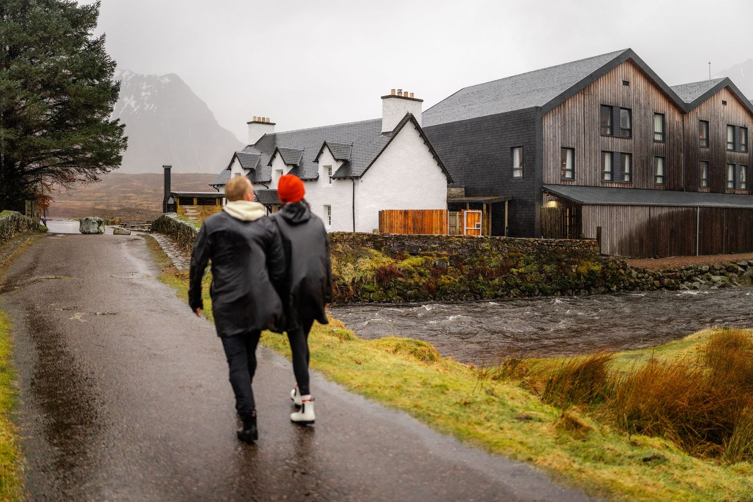 A couple walking along a path near traditional Scottish houses on a cloudy day.