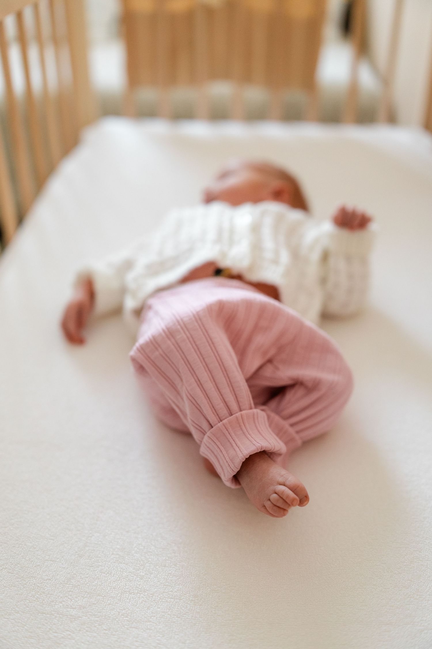 Baby wearing pink clothing lying on a white crib mattress.