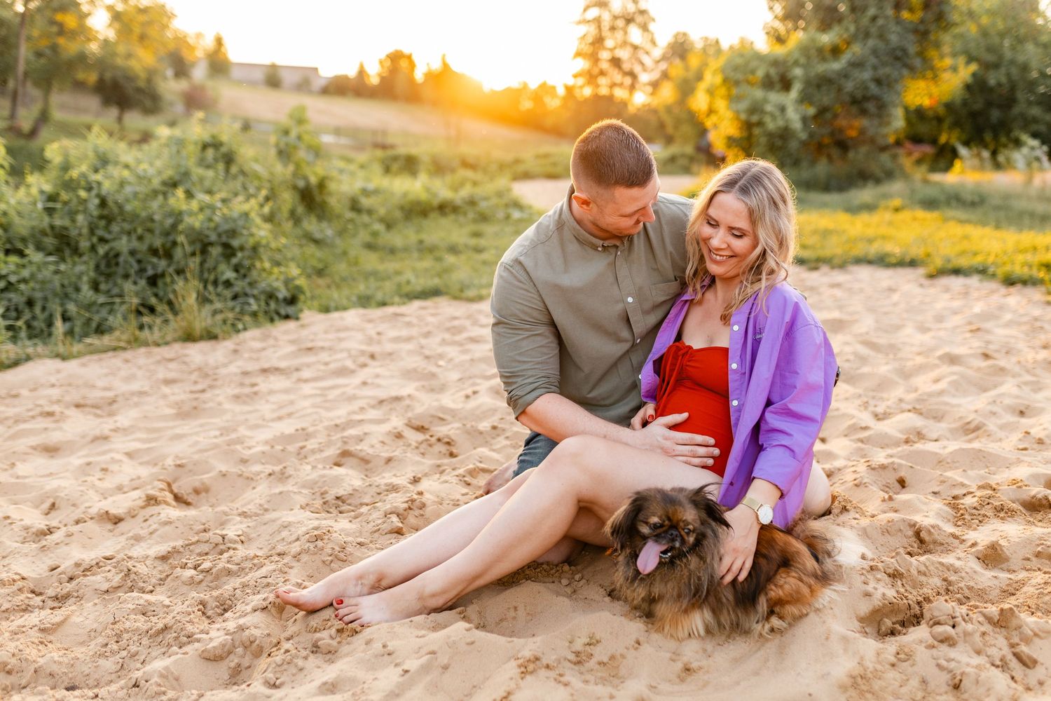 Couple relaxing on sandy beach with dog during golden hour.