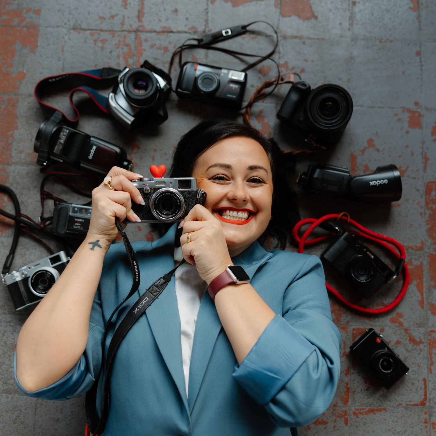 Professional camera operator in blue suit holds video equipment against industrial concrete wall background.