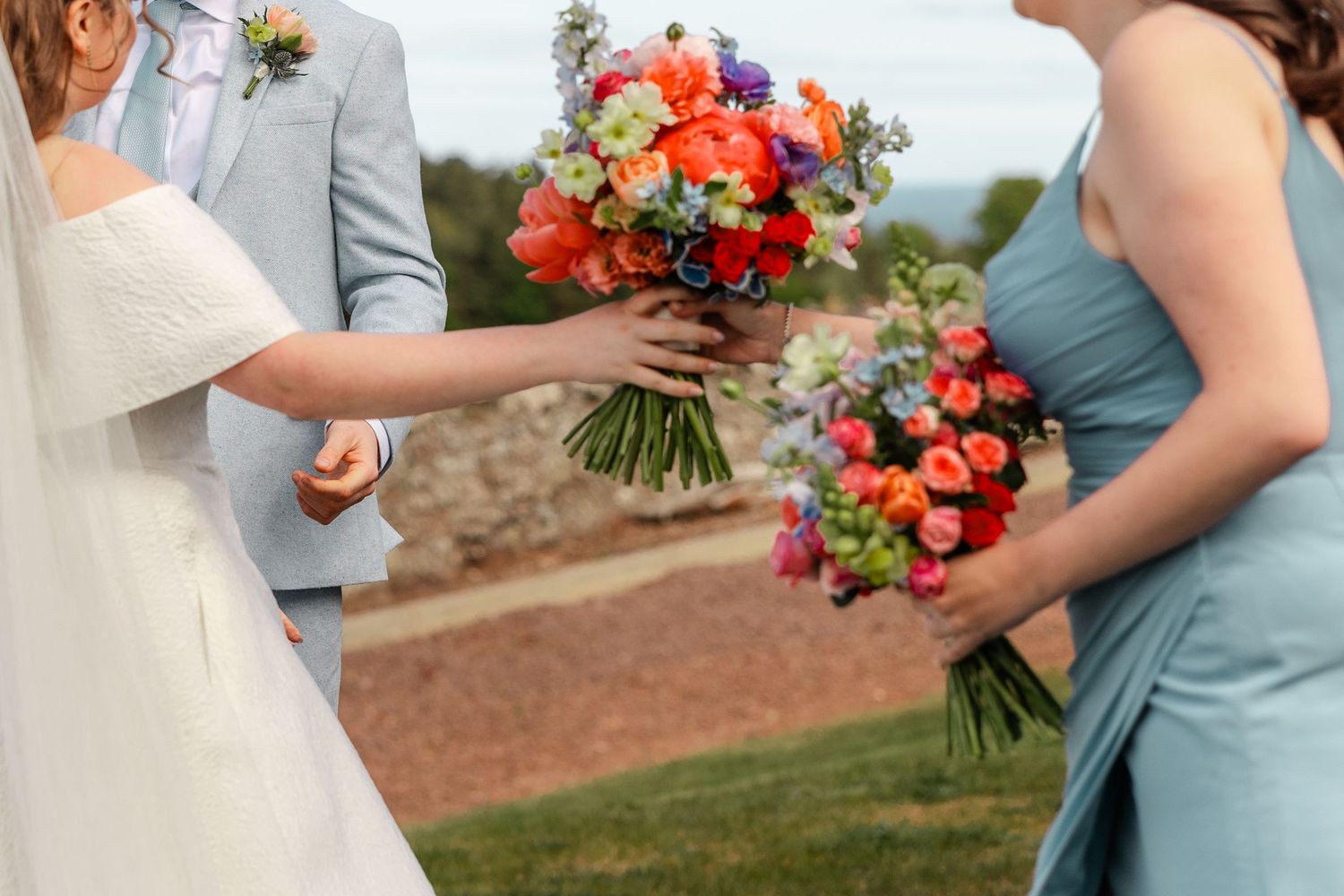 Close-up of colorful wedding bouquets with orange and blue flowers being exchanged.