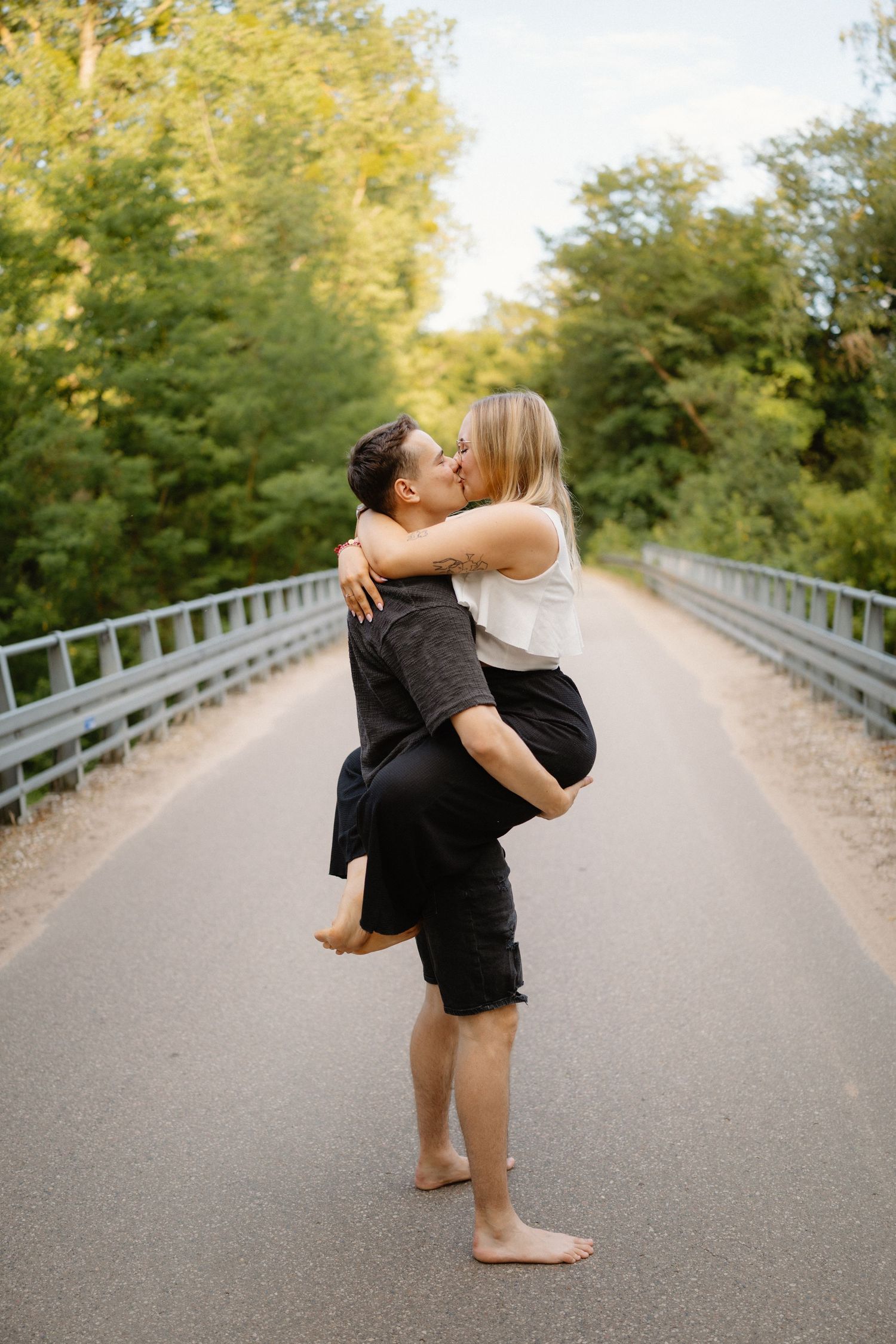 A couple shares a romantic moment on a tree-lined road during golden hour.