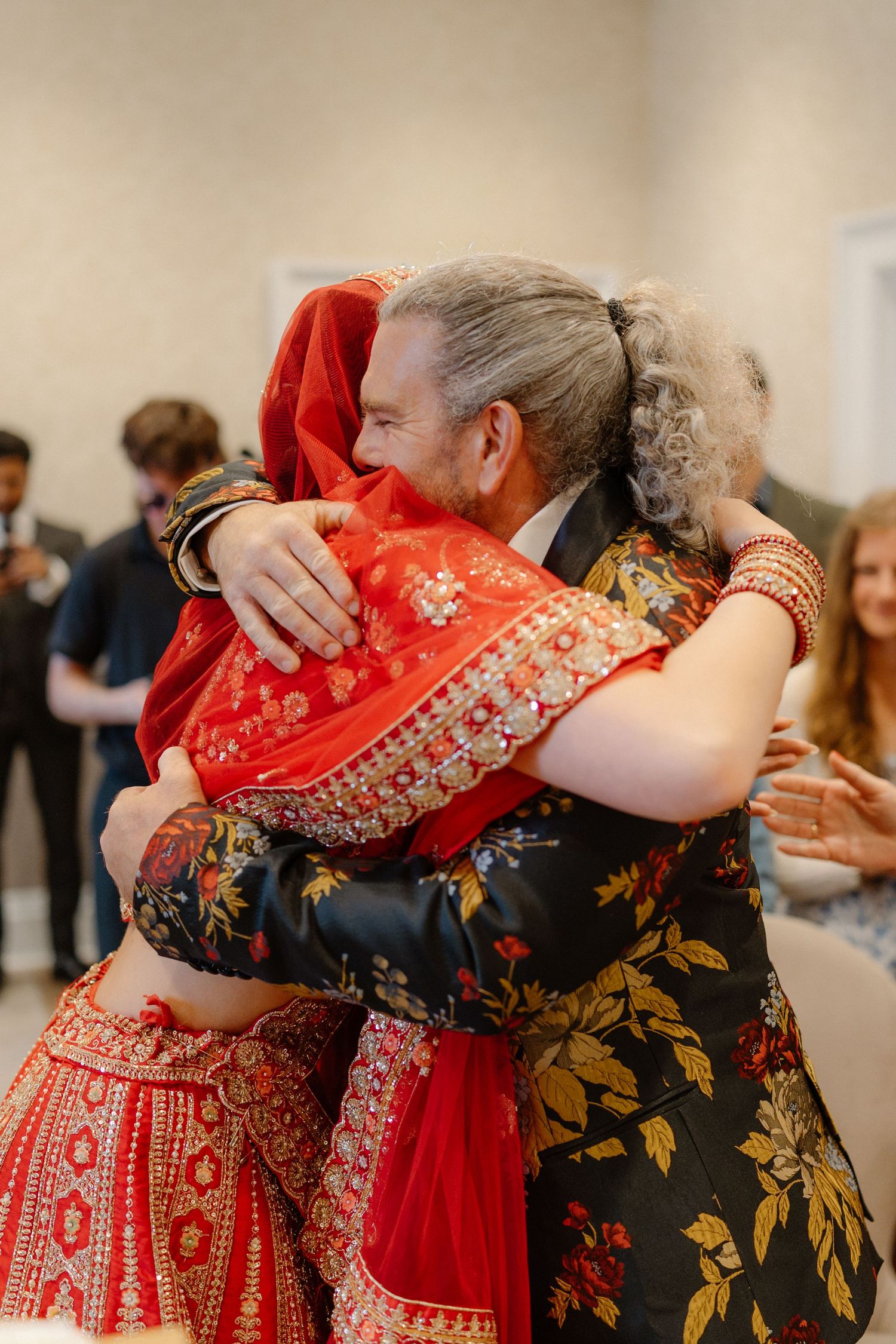 Emotional group hug between guests in colorful traditional Indian wedding attire.