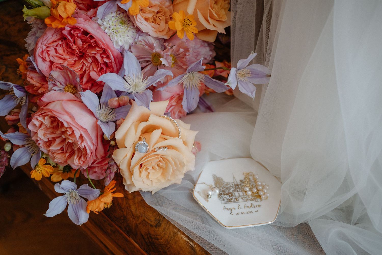 Colorful wedding bouquet with pink peonies and lavender flowers beside a personalized ring box and bridal veil.