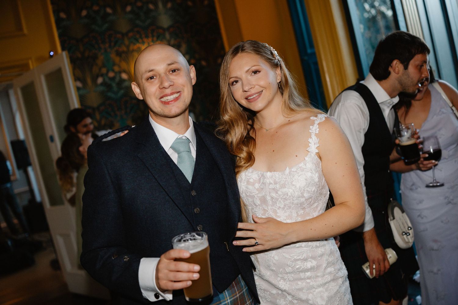 Bride and groom in Scottish kilt smiling together at wedding reception indoors.
