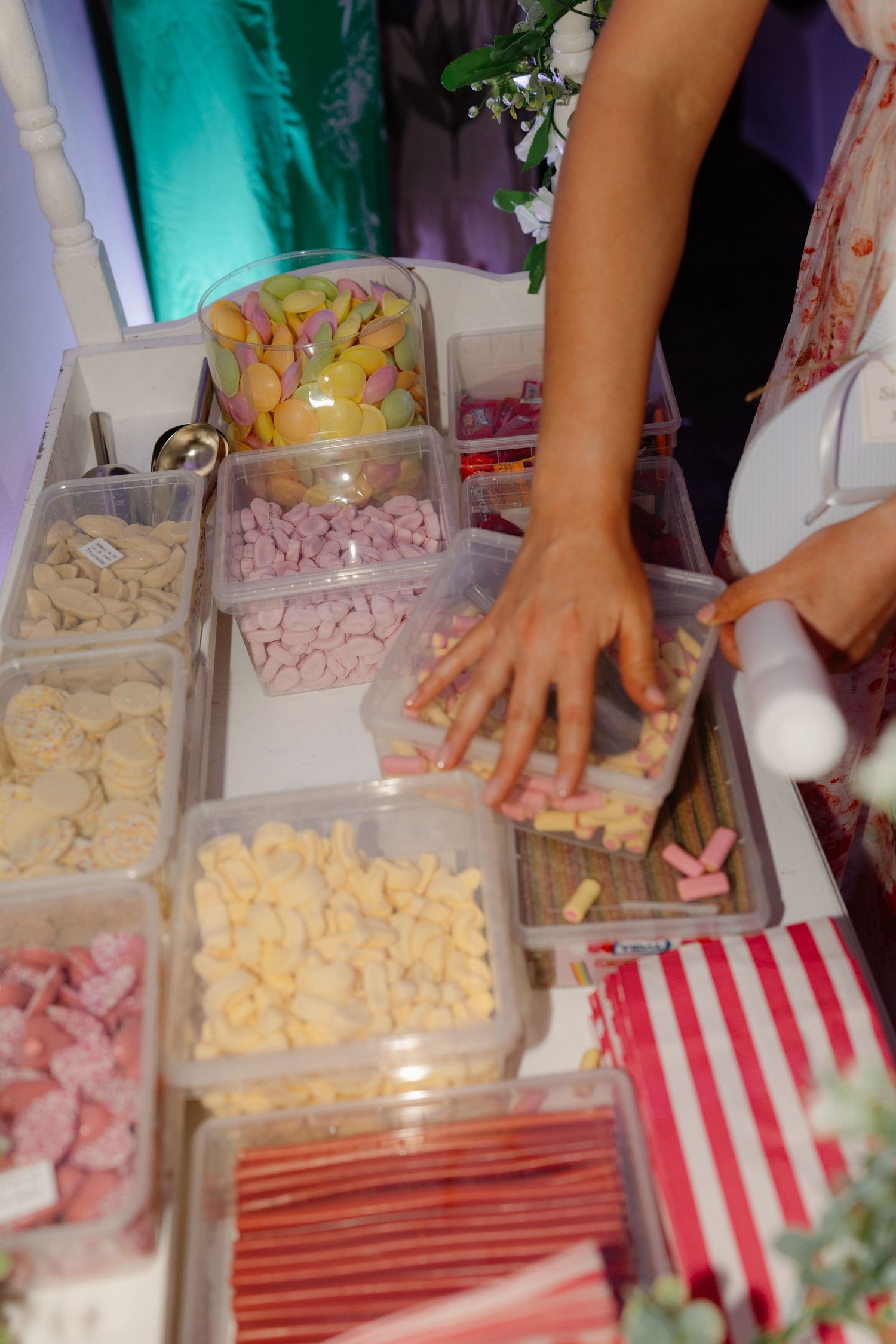 Hands reaching into plastic containers filled with colorful assorted sweets and candies at a wedding candy buffet.