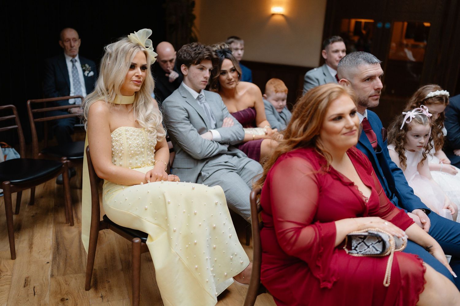Wedding guests seated during a ceremony, including a woman in yellow dress and another in red.
