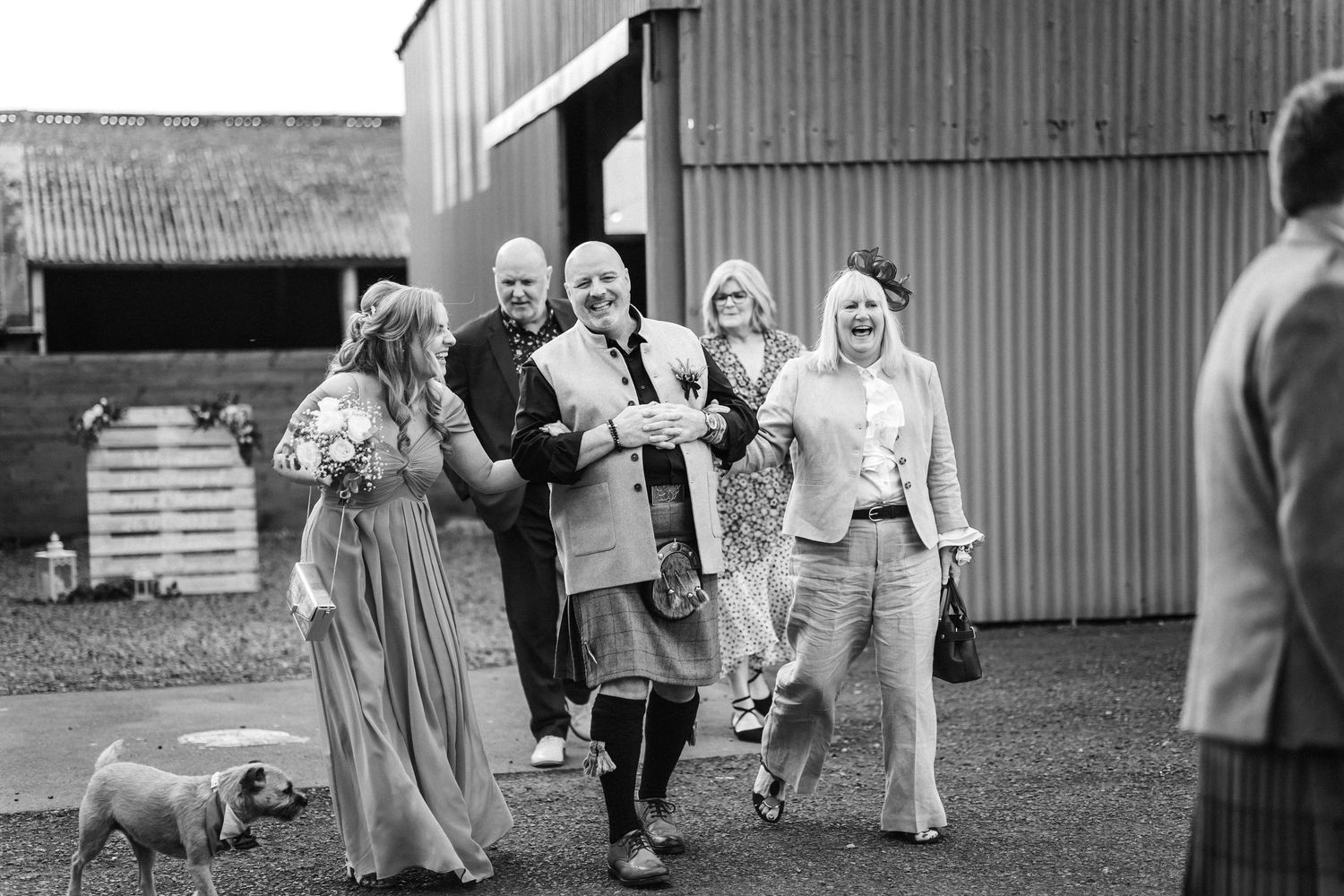 People walking and running together in black and white near a barn structure.