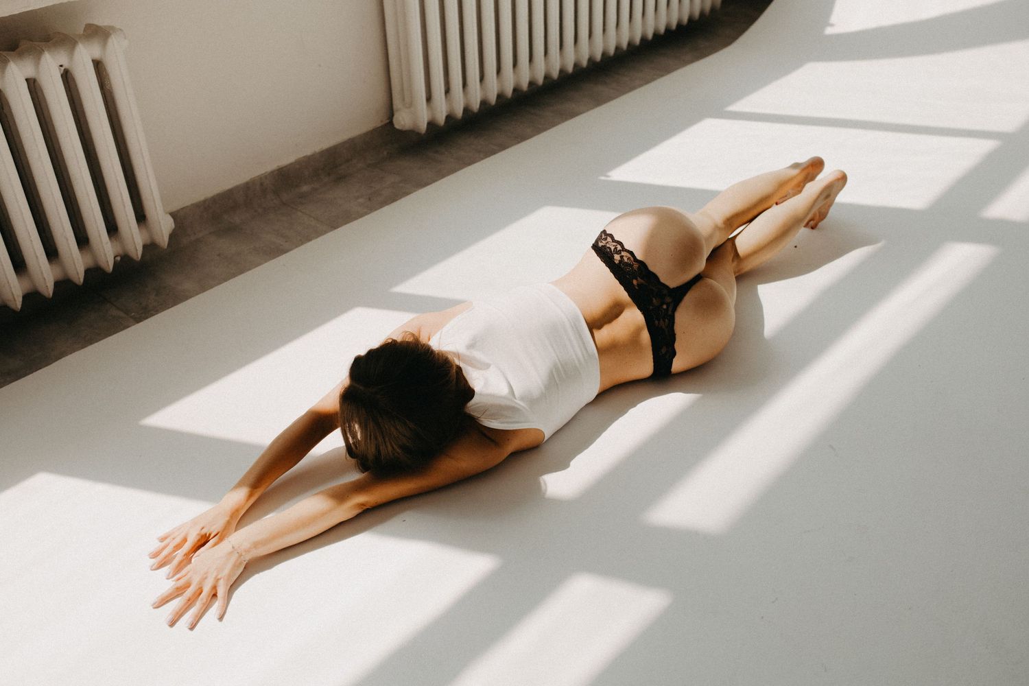 Artistic boudoir photography with dramatic window light casting shadows on white floor.