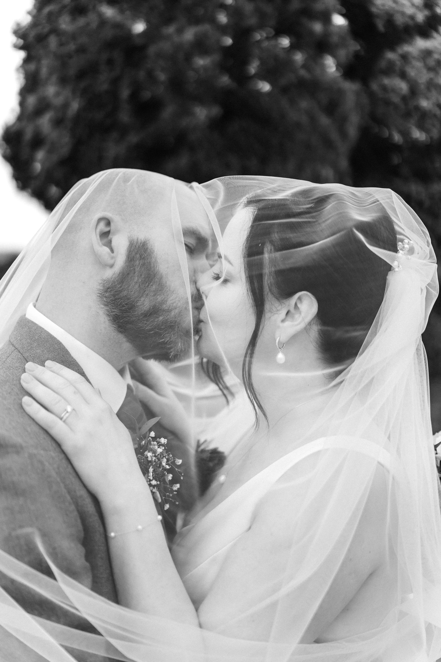 Romantic black and white series of newlyweds sharing intimate moments under flowing white veil.
