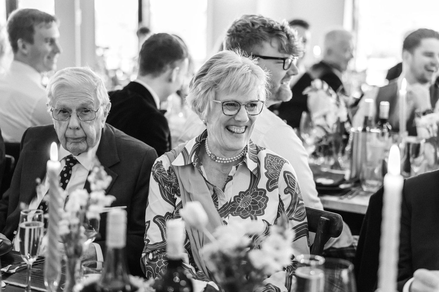Black and white photo of wedding guests laughing and socializing during reception dinner.