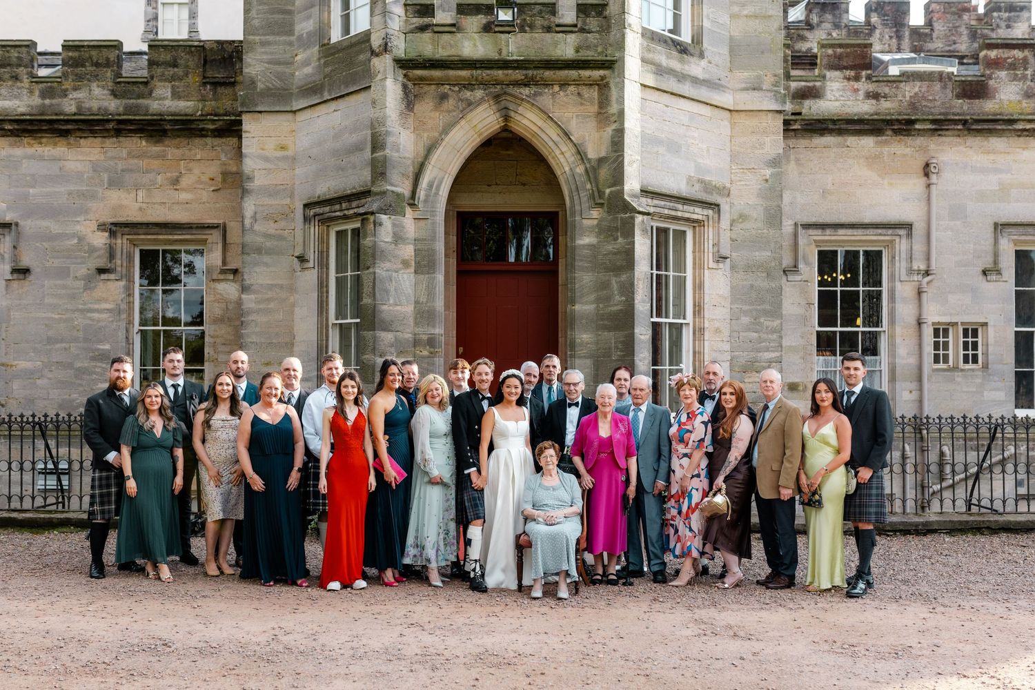 Wedding guests gathered in front of a historic stone castle building for formal group photos.