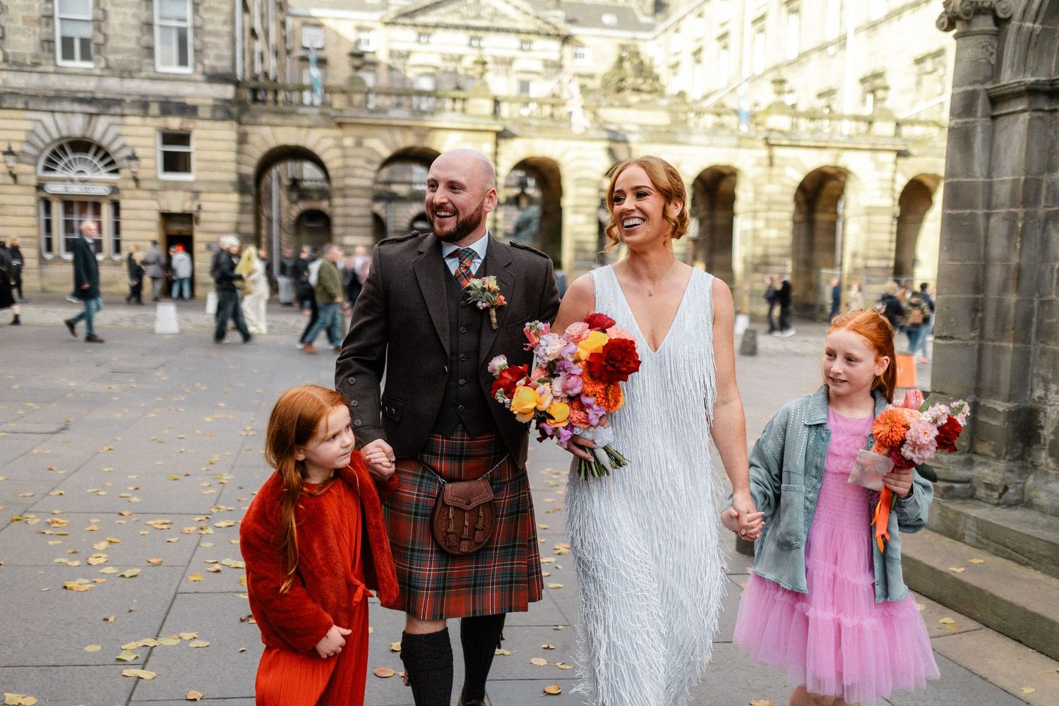 Wedding party poses on stone steps of historic building with autumn leaves scattered around.