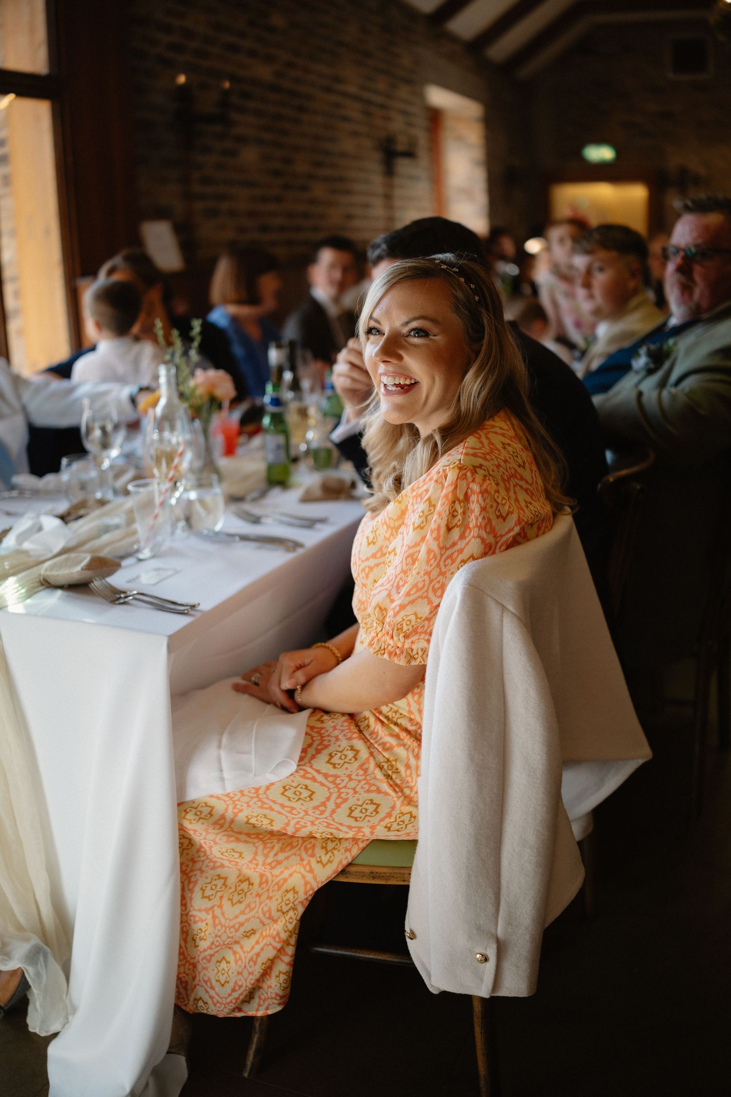 Wedding reception guests enjoying dinner at elegantly set tables in brick-walled venue.