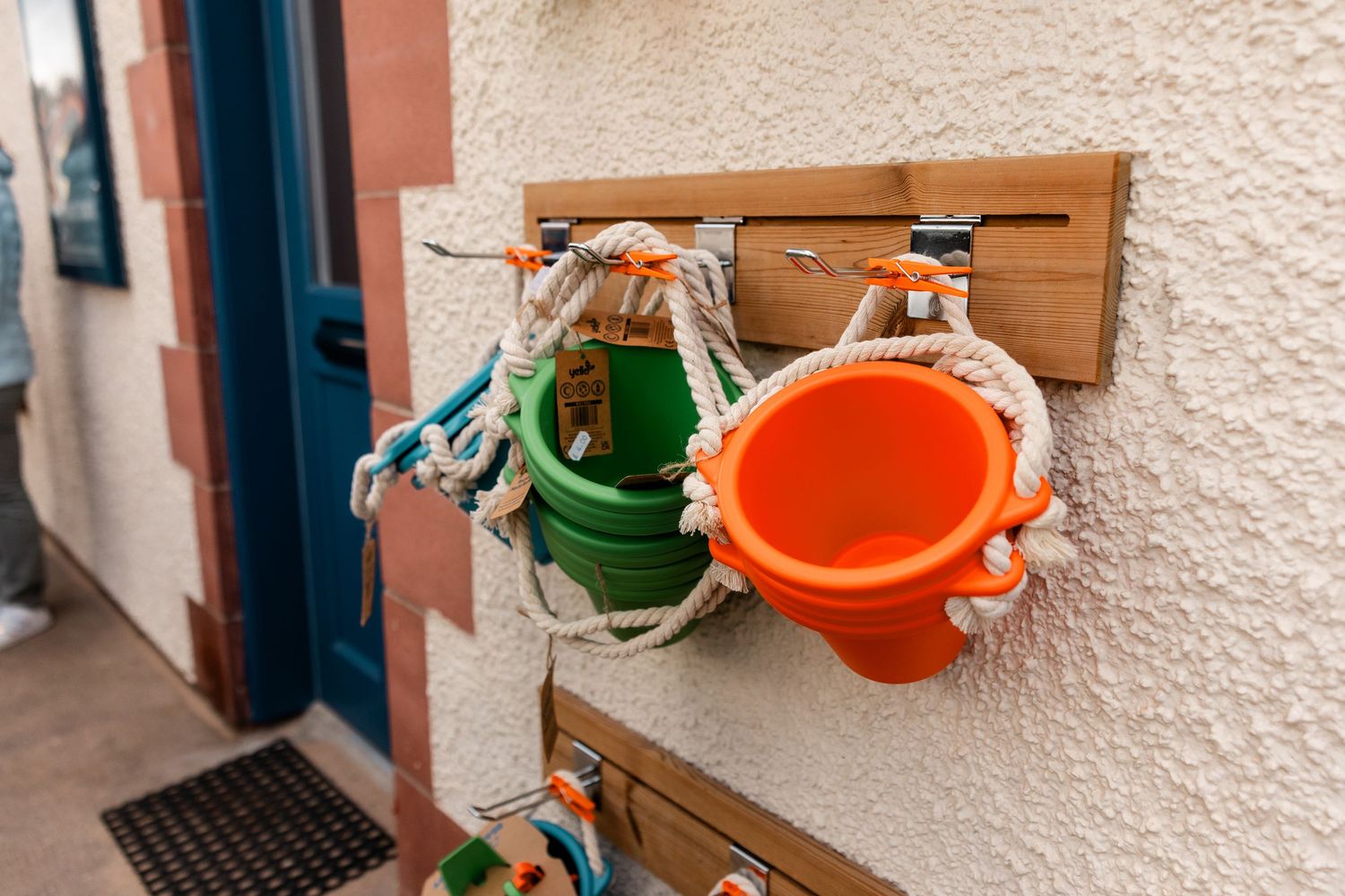 Rustic wooden shelves mounted on a textured wall with orange and green watering cans.