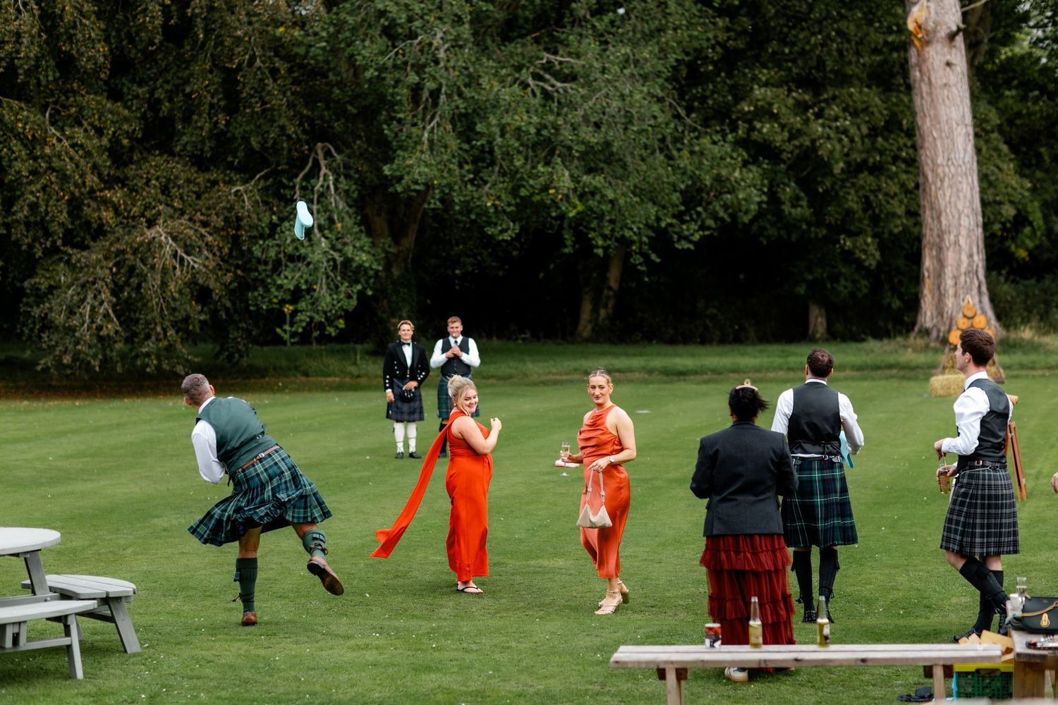 Wedding guests in kilts and colorful attire play lawn games on green grounds during outdoor reception.