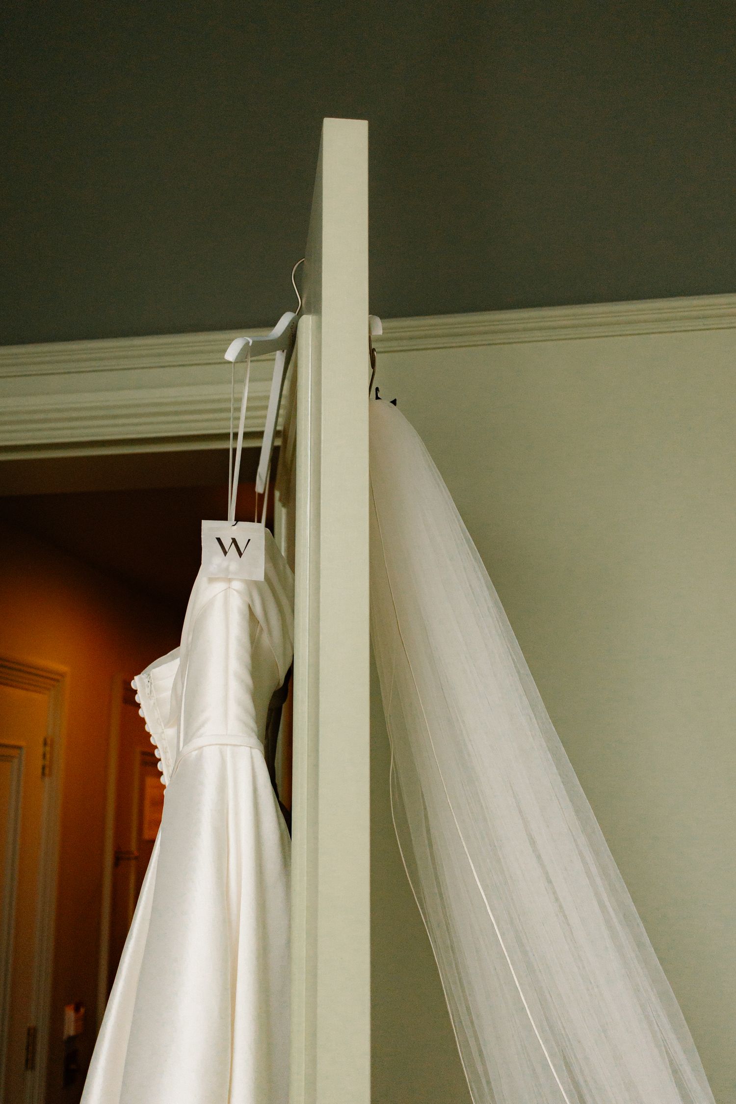White wedding dress and veil hanging on a door frame with a monogram hanger in a bridal suite.