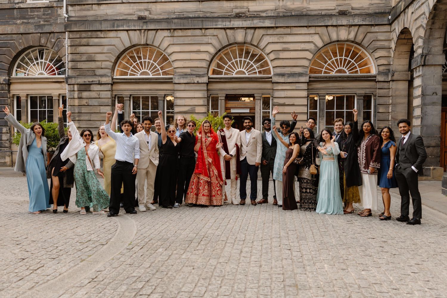 Wedding party group photo outside a historic stone building in Edinburgh, Scotland.
