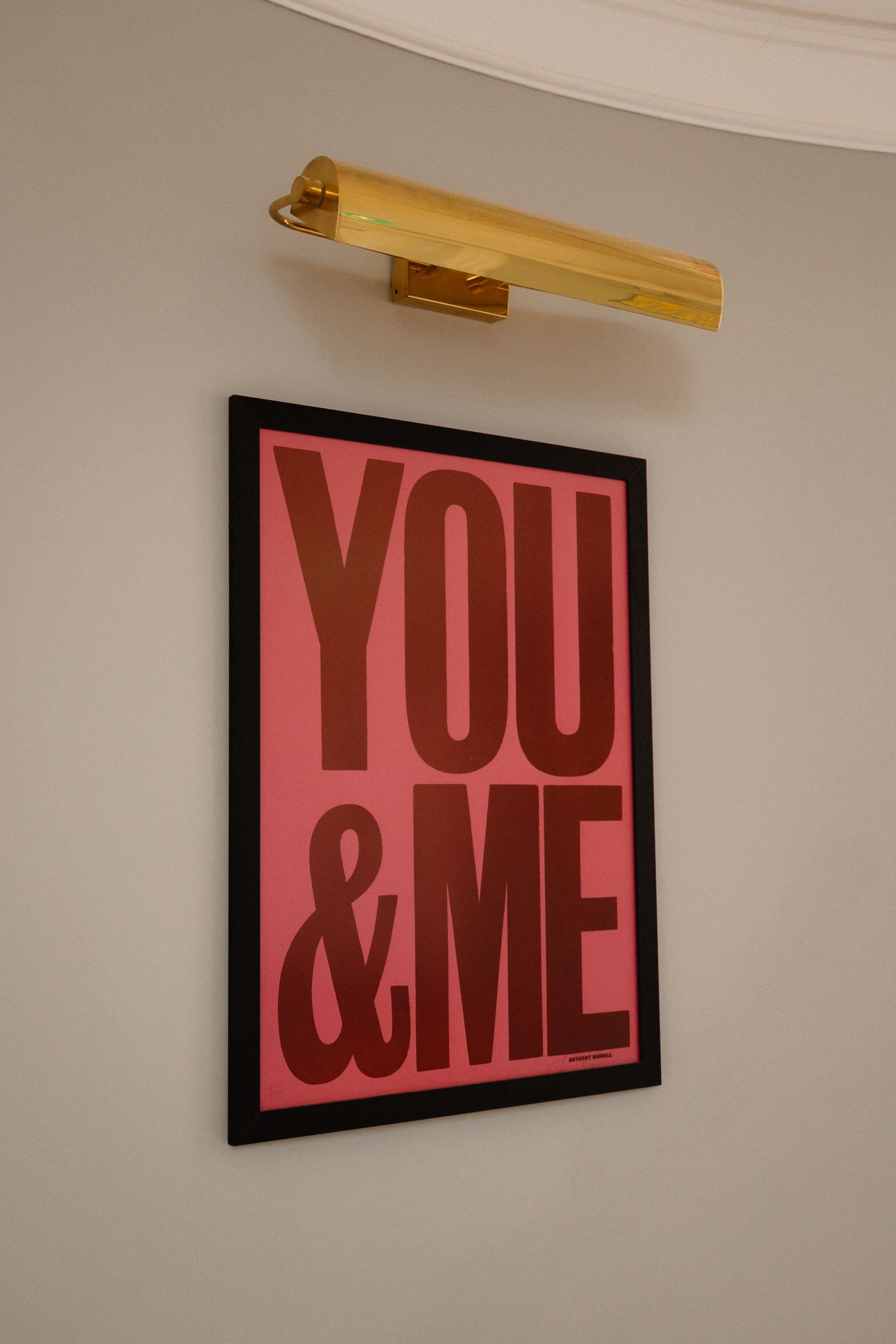 A series of four photos showing a pink and black text art installation reading 'YOU & ME' mounted on a white wall.