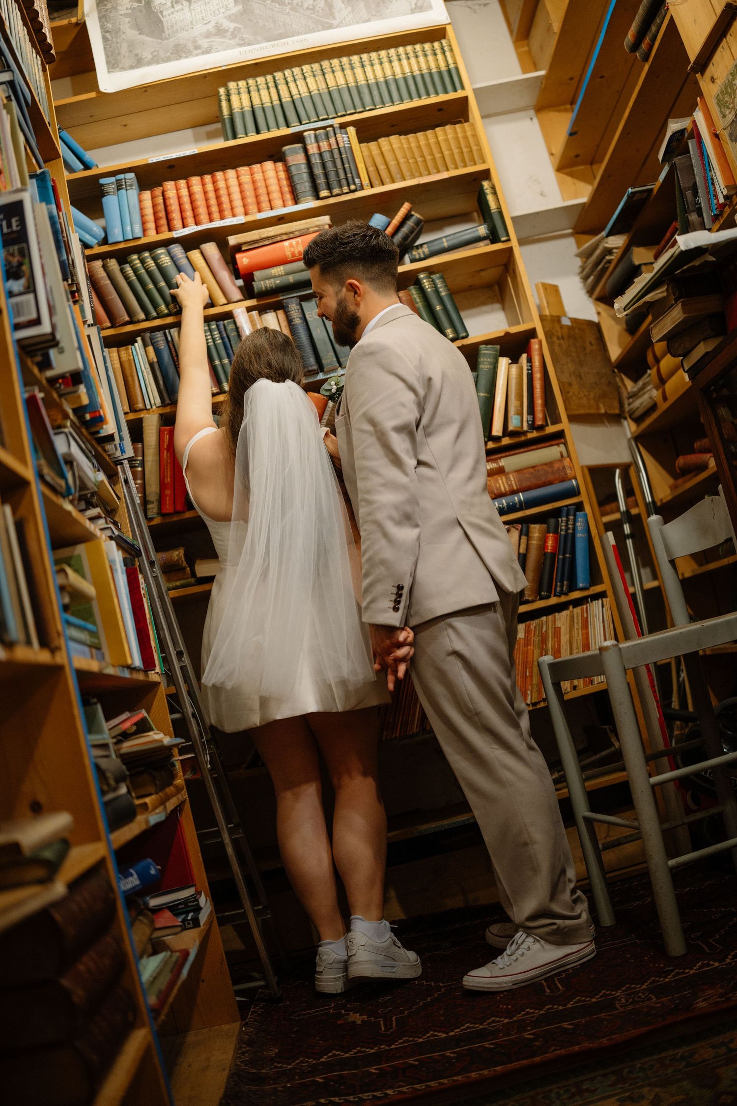 Couple in formal attire browsing through library bookshelves.