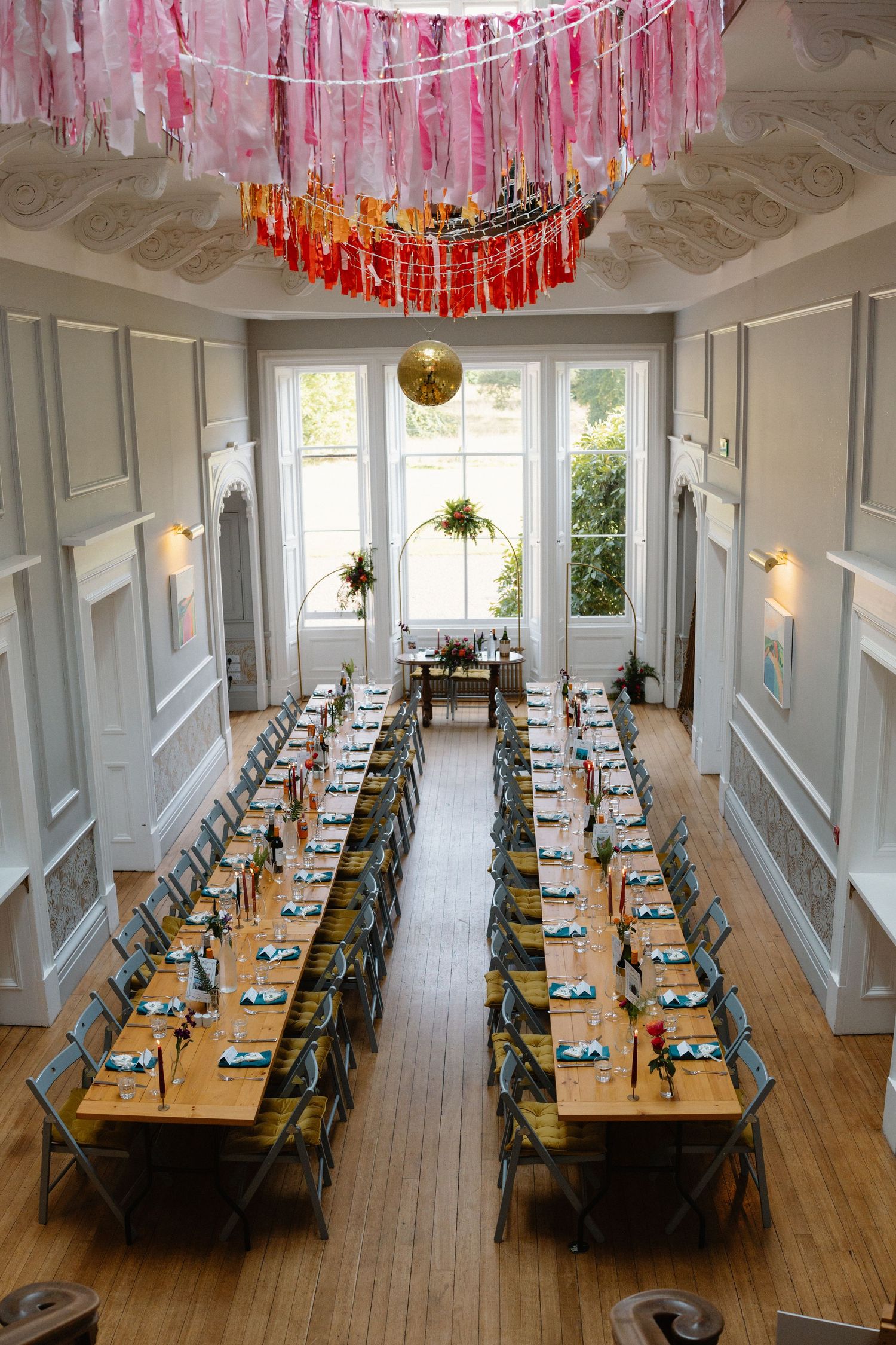 Wedding reception hall with long tables and pink streamers hanging from the ceiling.