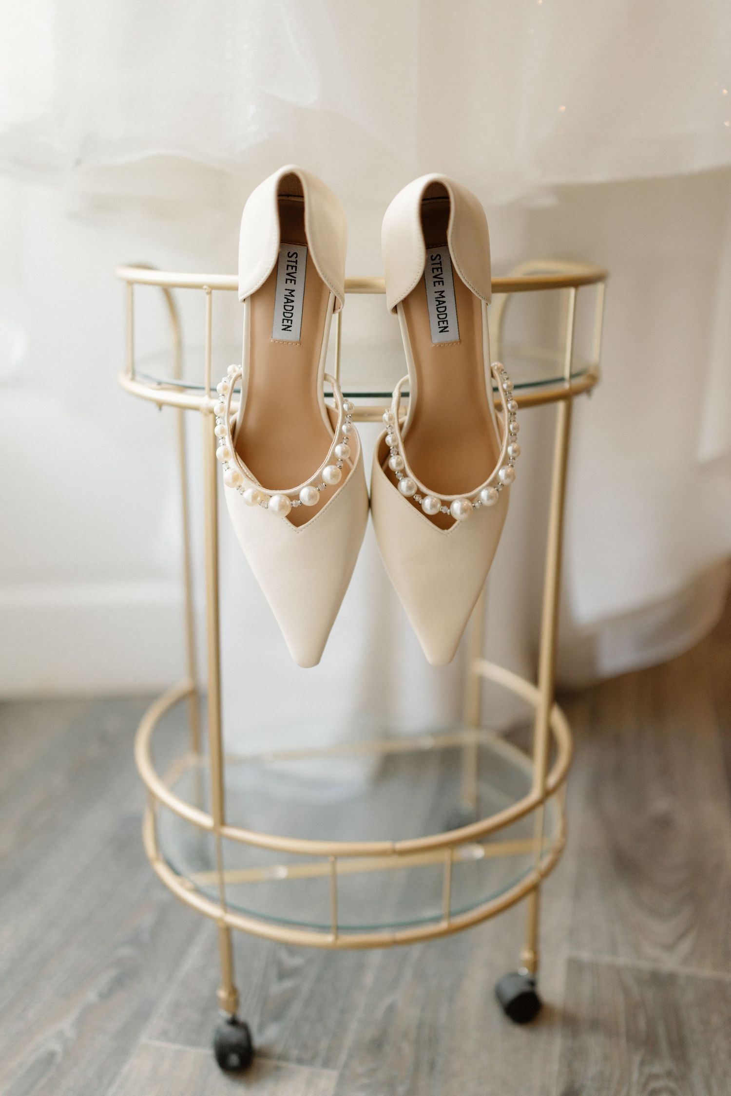 Elegant Steve Madden ivory pearl-embellished pointed-toe bridal flats displayed on a gold bar cart.