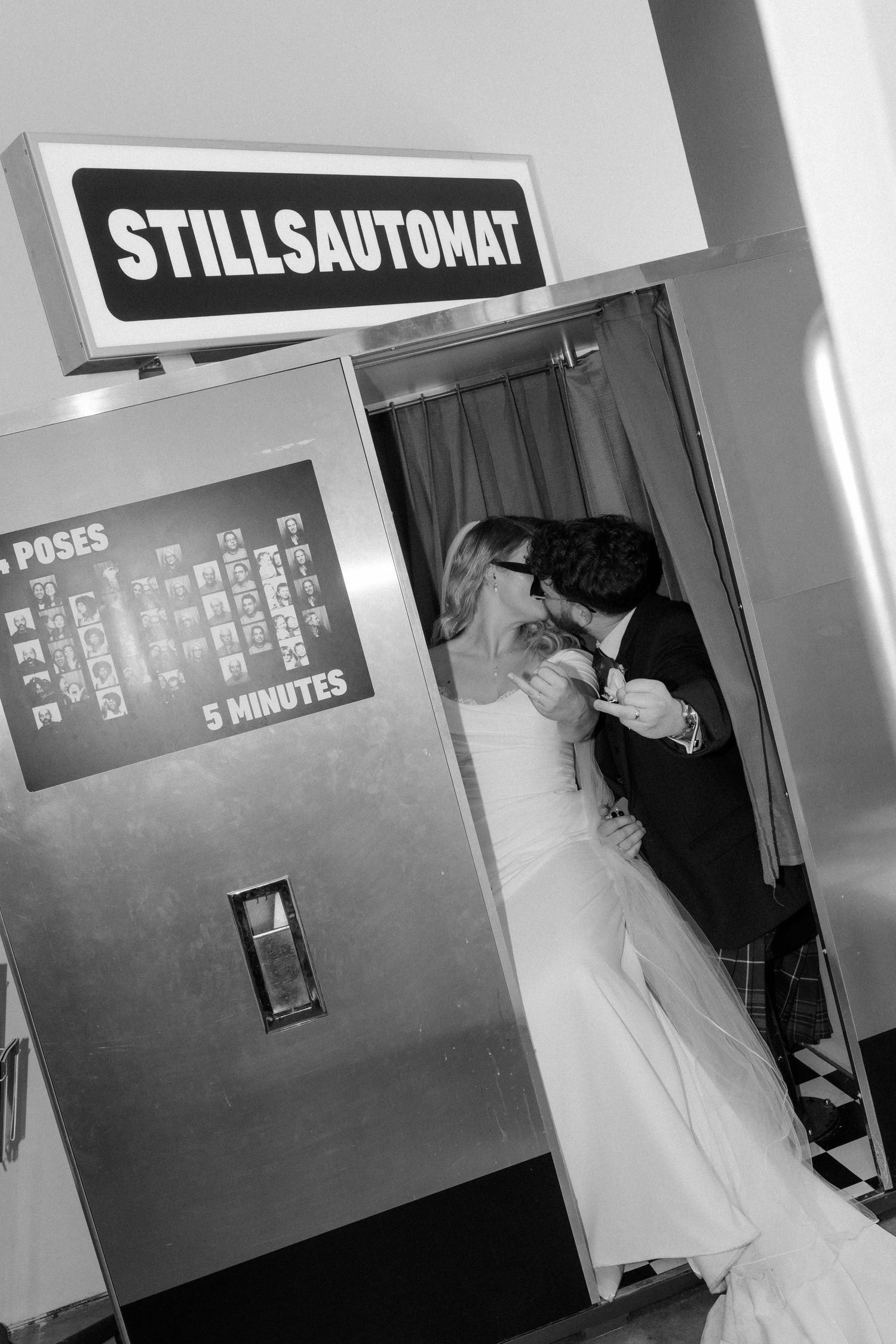Bride and groom share a kiss inside a vintage Stillsautomat photo booth in black and white.