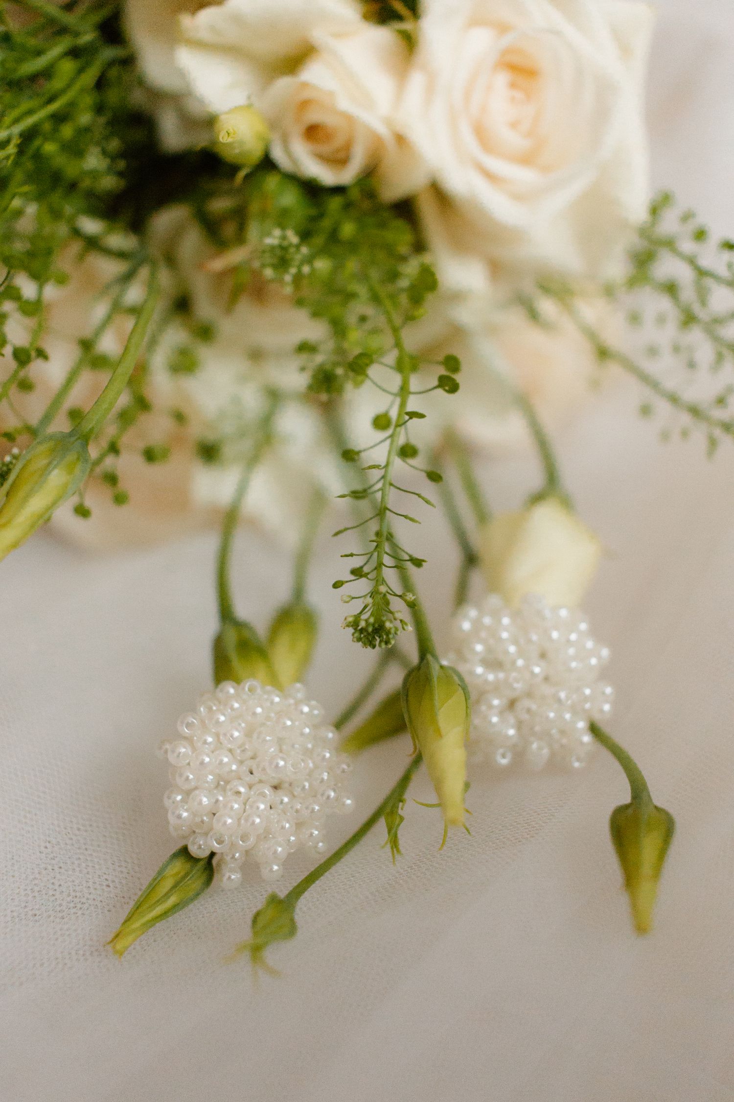 Elegant wedding bouquet with white roses and pearl-adorned flower buds on white fabric.