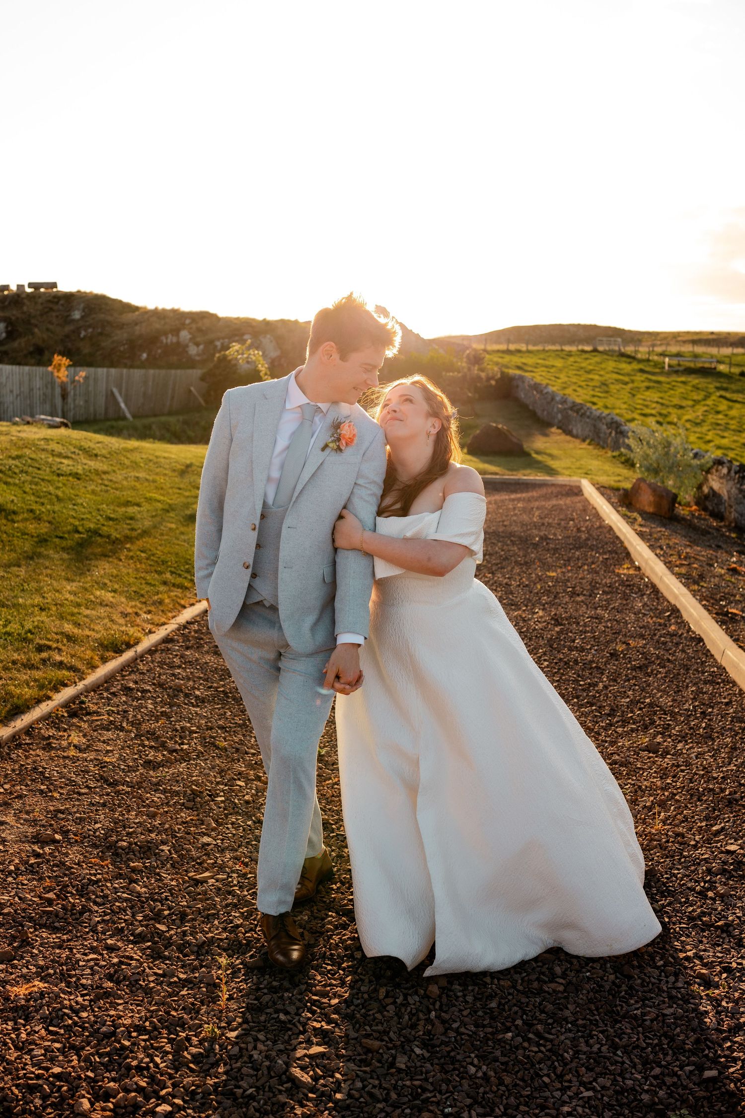 Happy bride and groom walk hand in hand at sunset, laughing together on their wedding day.