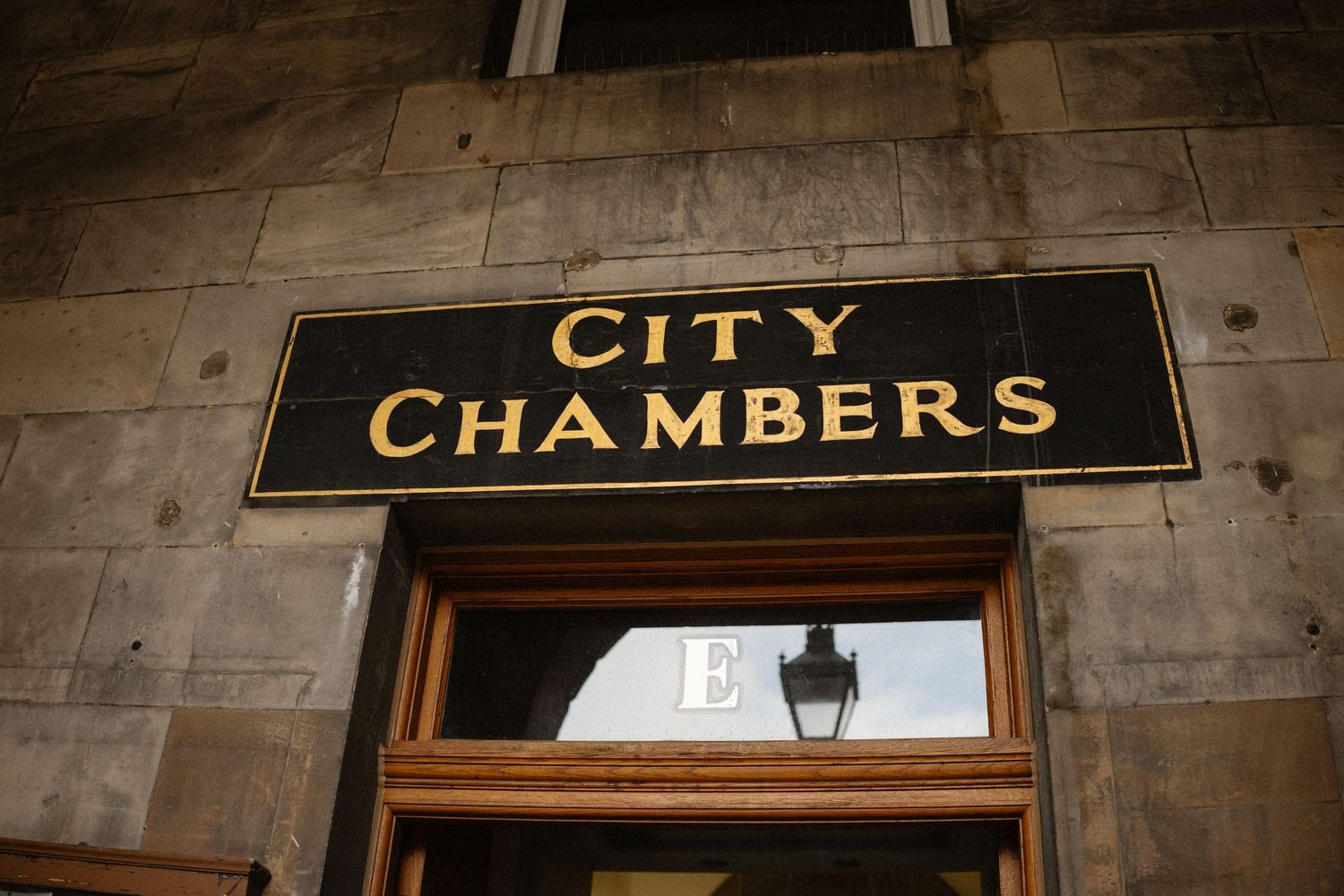 Gold lettering City Chambers sign mounted on stone wall above a wooden door entrance.