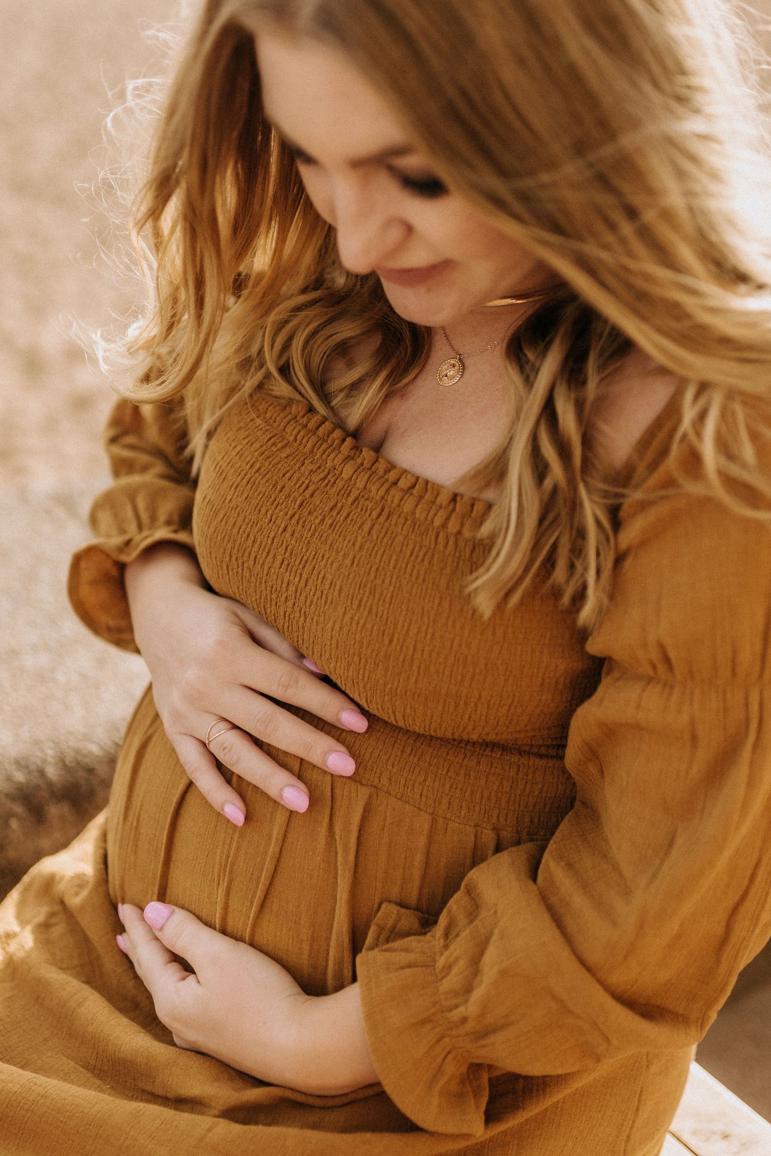Close-up of a woman in a brown dress cradling her pregnant belly.