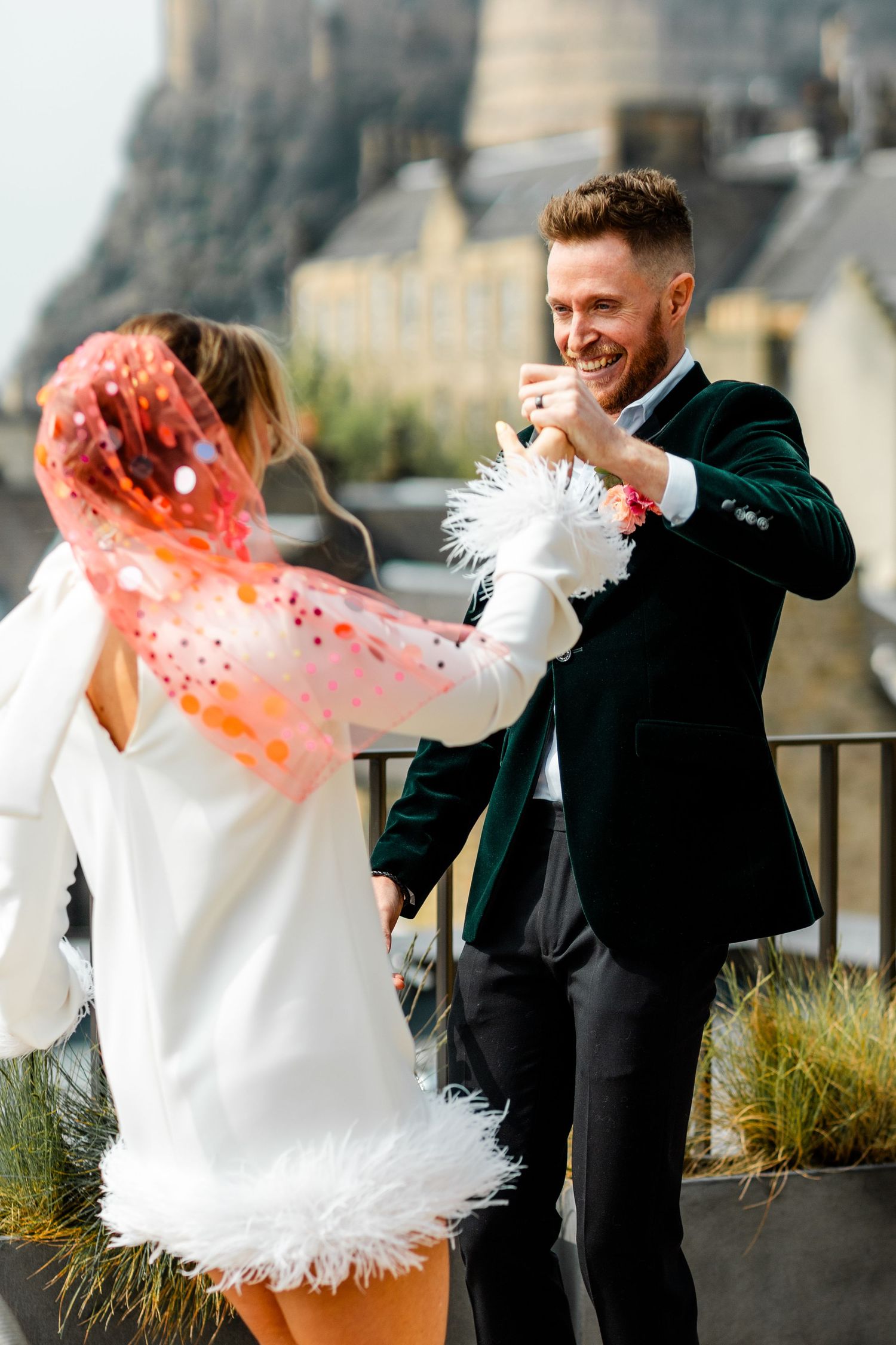 Couple shares a joyful dance outdoors with a white feathered shawl creating movement in the sunlight.
