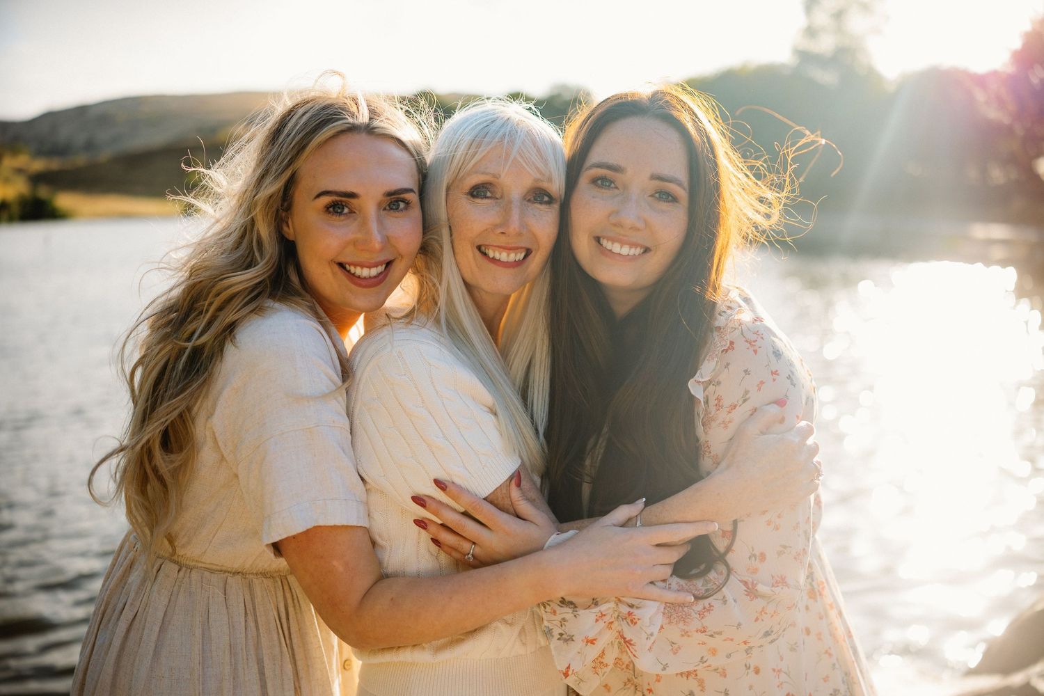 Three friends embrace and laugh together outdoors during golden hour sunset.