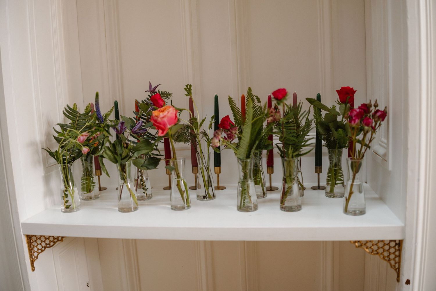 Red roses displayed in individual glass vases line a white shelf creating an elegant floral arrangement.