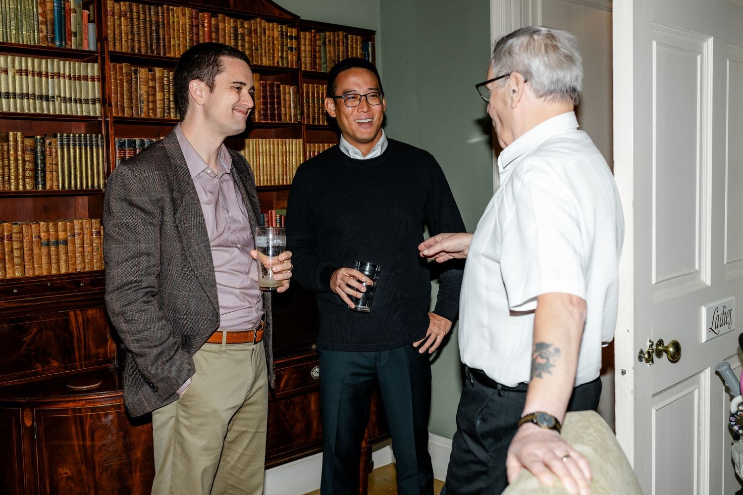 People engaged in conversation in a library setting with wooden bookshelves in the background.