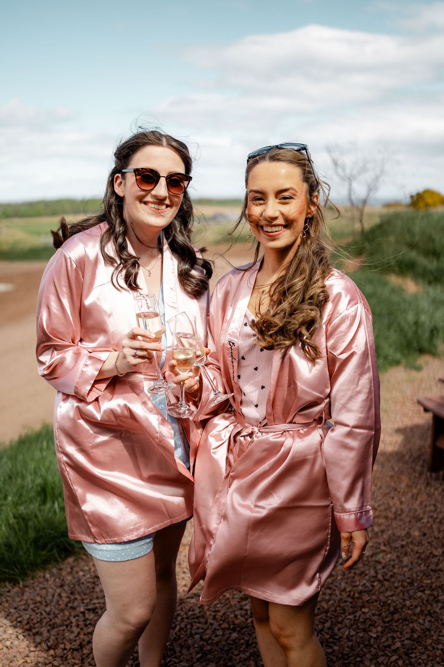 Two friends in matching pink satin robes sharing drinks outdoors.