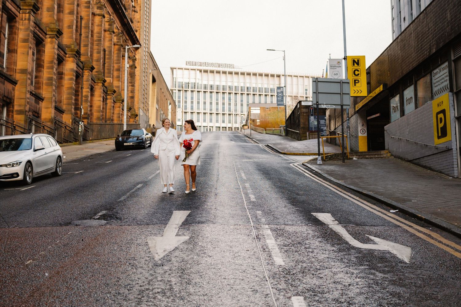 Bride and groom walking hand in hand down an empty urban street in Glasgow city centre on their wedding day.