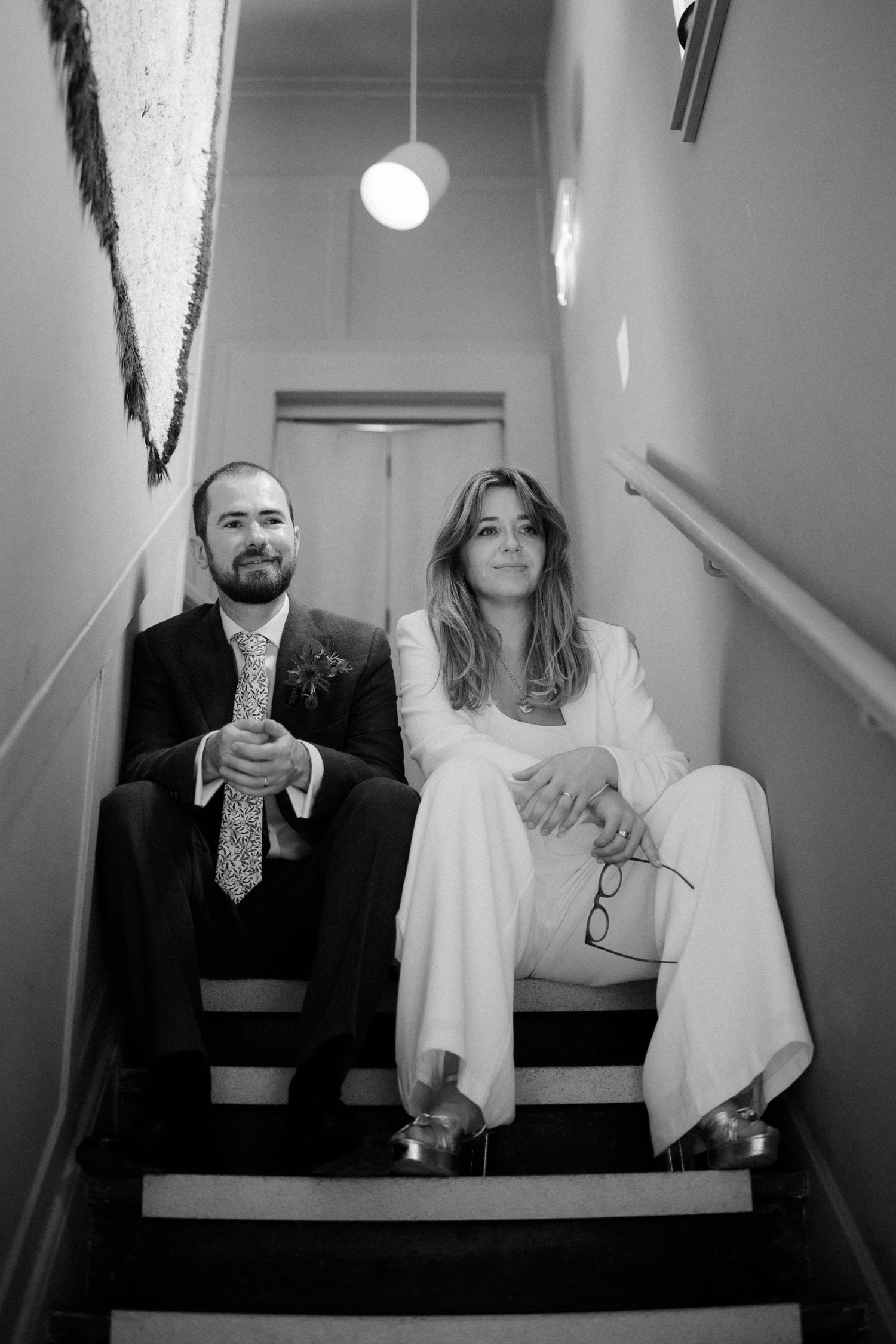 Bride and groom sitting together on staircase in black and white wedding photo.