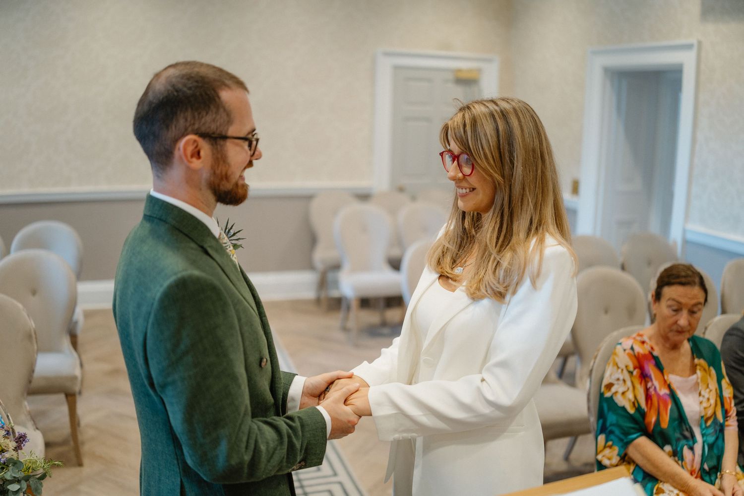 Bride and groom exchange vows holding hands during intimate wedding ceremony in elegant room.